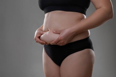 Gri arka planda göbek yağına dokunan kadın, yakın plan. Aşırı kilolu