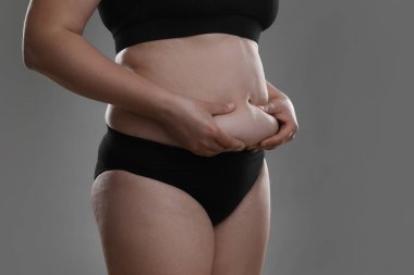 Gri arka planda göbek yağına dokunan kadın, yakın plan. Aşırı kilolu