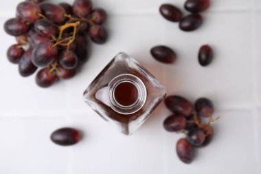 Cam şişede şarap sirkesi ve beyaz masada üzümler.