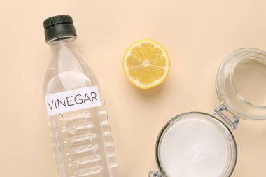 Eco friendly natural cleaners. Vinegar in bottle, cut lemon and jar of soda on beige background, flat lay