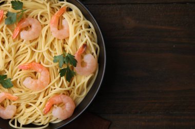 Tasty spaghetti with shrimps and parsley in bowl on wooden table, top view. Space for text
