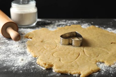 Making shortcrust pastry. Raw dough, flour, cookie cutter and rolling pin on grey table, closeup