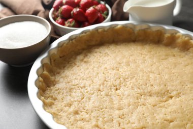 Kısa hamur işi yapıyorum. Pişirme kabında çiğ hamur, şeker ve çilek gri masada, yakın plan.