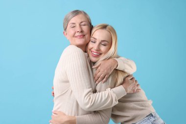 Family portrait of young woman and her mother on light blue background