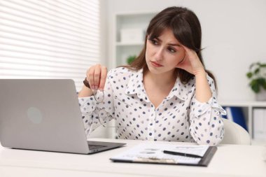 Overwhelmed woman sitting at table with laptop in office