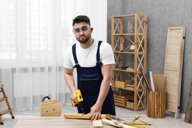 Genç işçi atölyedeki masada elektrikli matkap kullanıyor.