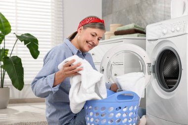 Happy housewife with laundry basket near washing machine at home