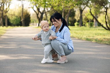 Anne, o dışarıda yürümeyi öğrenirken bebeğine bakıyor.