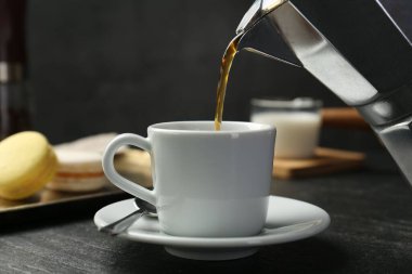 Moka pot 'tan koyu dokulu masada fincana kahve dökmek, yakın çekim.