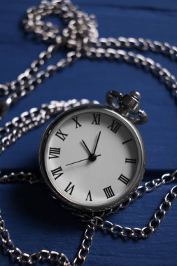 Mavi ahşap masada zincirli gümüş cep saati, yakın plan.