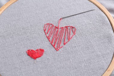 İşlemeli kırmızı kalpler ve açık gri kumaş üzerinde iğne, yakın plan.