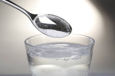Işık arkaplanındaki su bardağına kabartma tozu eklemek, yakın plan