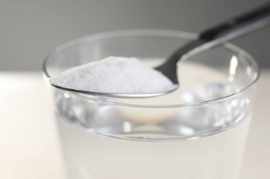 Renkli arka planda kabartma tozu olan bir bardak su ve kaşık, yakın plan.