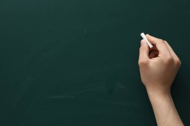Teacher writing with chalk on green chalkboard, closeup. Space for text
