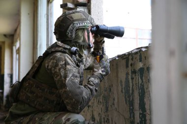 Military mission. Soldier in uniform with binoculars inside abandoned building