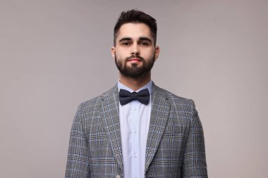 Portrait of handsome man in suit, shirt and bow tie on grey background