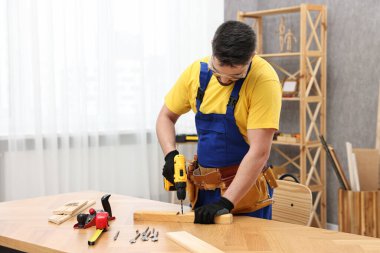 Genç işçi atölyedeki masada elektrikli matkap kullanıyor.