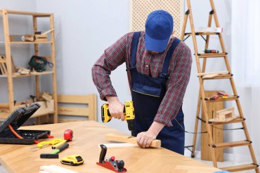 Genç işçi atölyedeki masada elektrikli matkap kullanıyor.