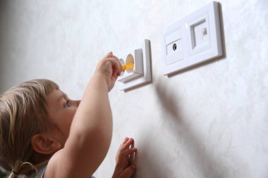 Evde oyuncak tornavida ve prizle oynayan küçük bir çocuk, yakın plan. Tehlikeli bir durum.