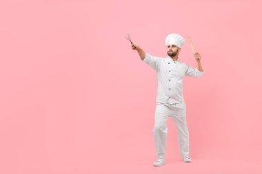 Professional chef holding kitchen utensils and having fun on pink background. Space for text