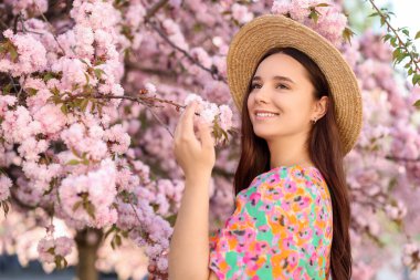 Hasır şapkalı güzel kadın bahar günü çiçek açan ağacın yanında.