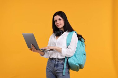 Student with laptop and backpack on yellow background