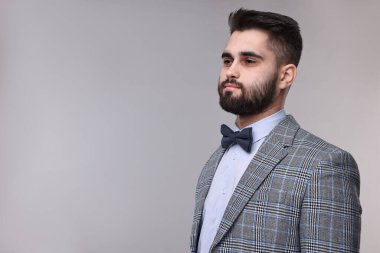 Portrait of handsome man in suit, shirt and bow tie on grey background. Space for text