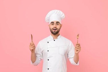 Profesyonel aşçı pembe arka planda mutfak aletleri tutuyor.