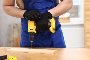 Atölyede elektrikli matkap kullanan genç işçi, yakın plan.