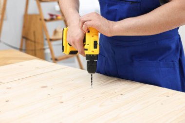 Atölyede elektrikli matkap kullanan genç işçi, yakın plan.