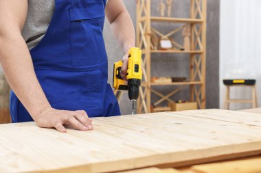 Atölyede elektrikli matkap kullanan genç işçi, yakın plan.