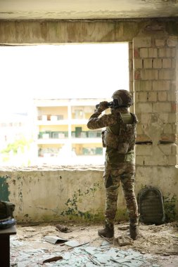Military mission. Soldier in uniform with binoculars inside abandoned building, back view clipart