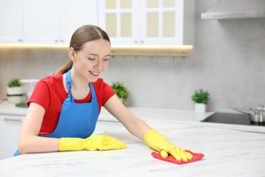Woman cleaning white marble table with rag in kitchen, space for text