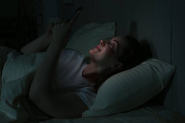Woman using smartphone on bed at night. Internet addiction