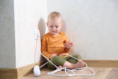 Little child playing with power strip near electrical socket at home. Dangerous situation