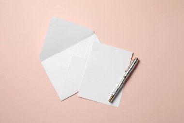 Boş kağıt, mektup zarfı ve bej arka planda kalem, üst manzara. Metin için boşluk