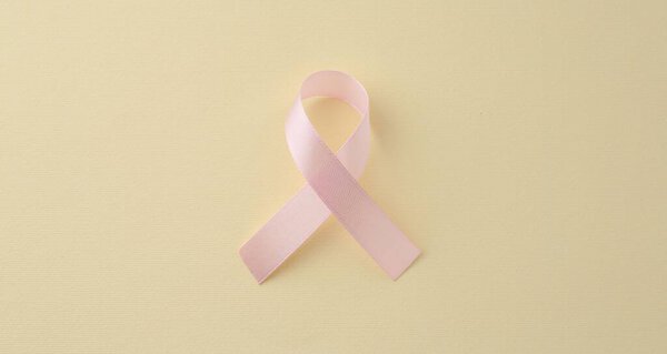 Pink awareness ribbon on pale yellow background, top view