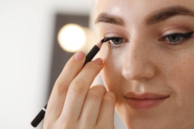 Makyaj ürünü. Kapalı alanda siyah göz kalemi kullanan kadın, yakın plan.