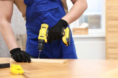 Atölyede elektrikli matkap kullanan genç işçi, yakın plan.