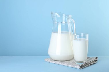 Açık mavi arka planda sürahi ve bir bardak taze süt, metin için boşluk