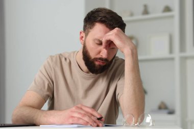 Overwhelmed man suffering from headache at table indoors