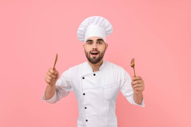 Profesyonel aşçı pembe arka planda mutfak aletleri tutuyor.