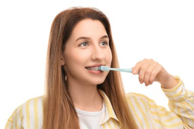 Smiling woman with dental braces cleaning teeth on white background
