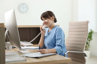 Smiling medical assistant talking by phone in office