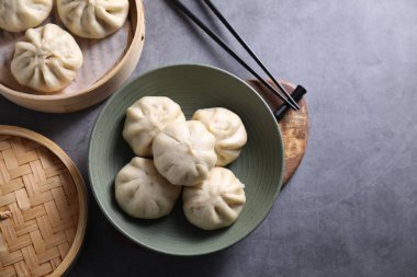 Lezzetli bao çörekleri (baozi) ve yemek çubukları gri masada, düz. Metin için boşluk