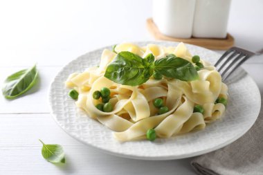 Delicious pasta with green peas served on white wooden table