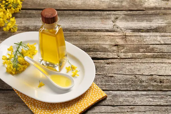 stock image Rapeseed oil in glass bottle, gravy boat and beautiful yellow flowers on wooden table, space for text