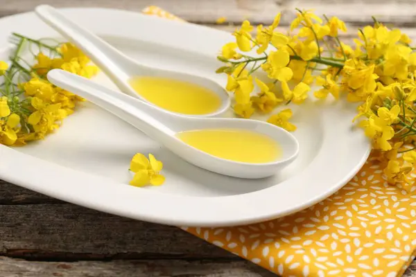 stock image Rapeseed oil in gravy boats and beautiful yellow flowers on wooden table, closeup