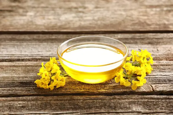 Stock image Rapeseed oil in glass bowl and beautiful yellow flowers on wooden table