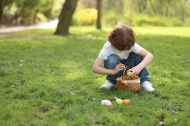 Easter celebration. Cute little boy hunting eggs outdoors, space for text